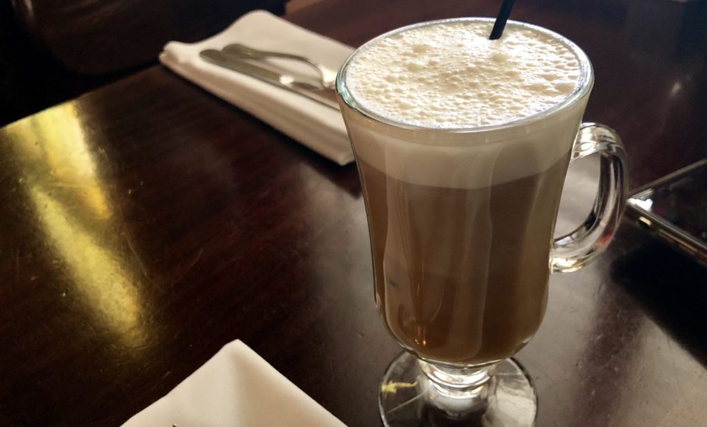 Irish coffee: a rich and dark coffee topped with a layer of creamy whipped cream. It's placed on a wooden table and surrounded by napkins and utensils 