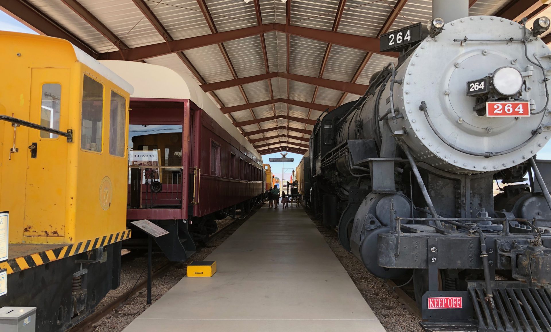 The Nevada State Railroad Museum walkaway where trains of various design and colors appear such as yellow, red and a vintage gray one
