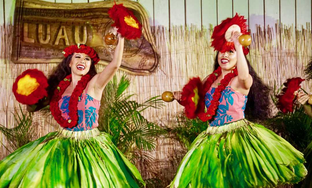 Two girls with flower crowns and green hula skirt doing a Hawaiian dance form expressing chant or song