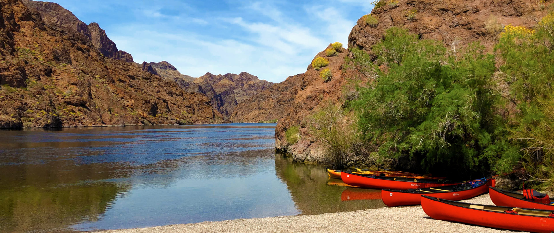 A view of a Las Vegas lake where bright red Kayaks are seen in front while rocky mountains are seen in the background