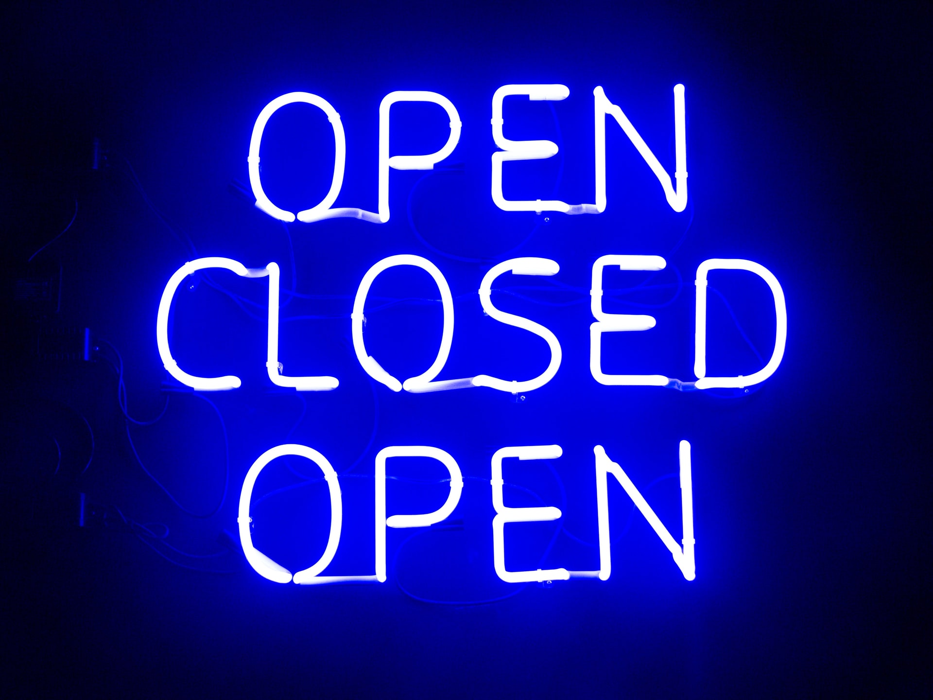 A LED Light sign that says Open Closed Open in blue lighting on a black background